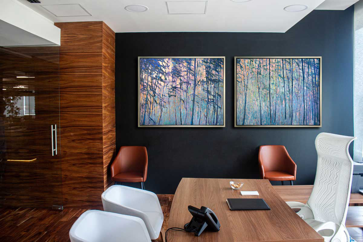 Two multicolored abstract tree landscape prints in silver floater frames hang on a dark blue wall above two brown leather chairs, a wooden desk, a tall white mesh chair and two white chairs.