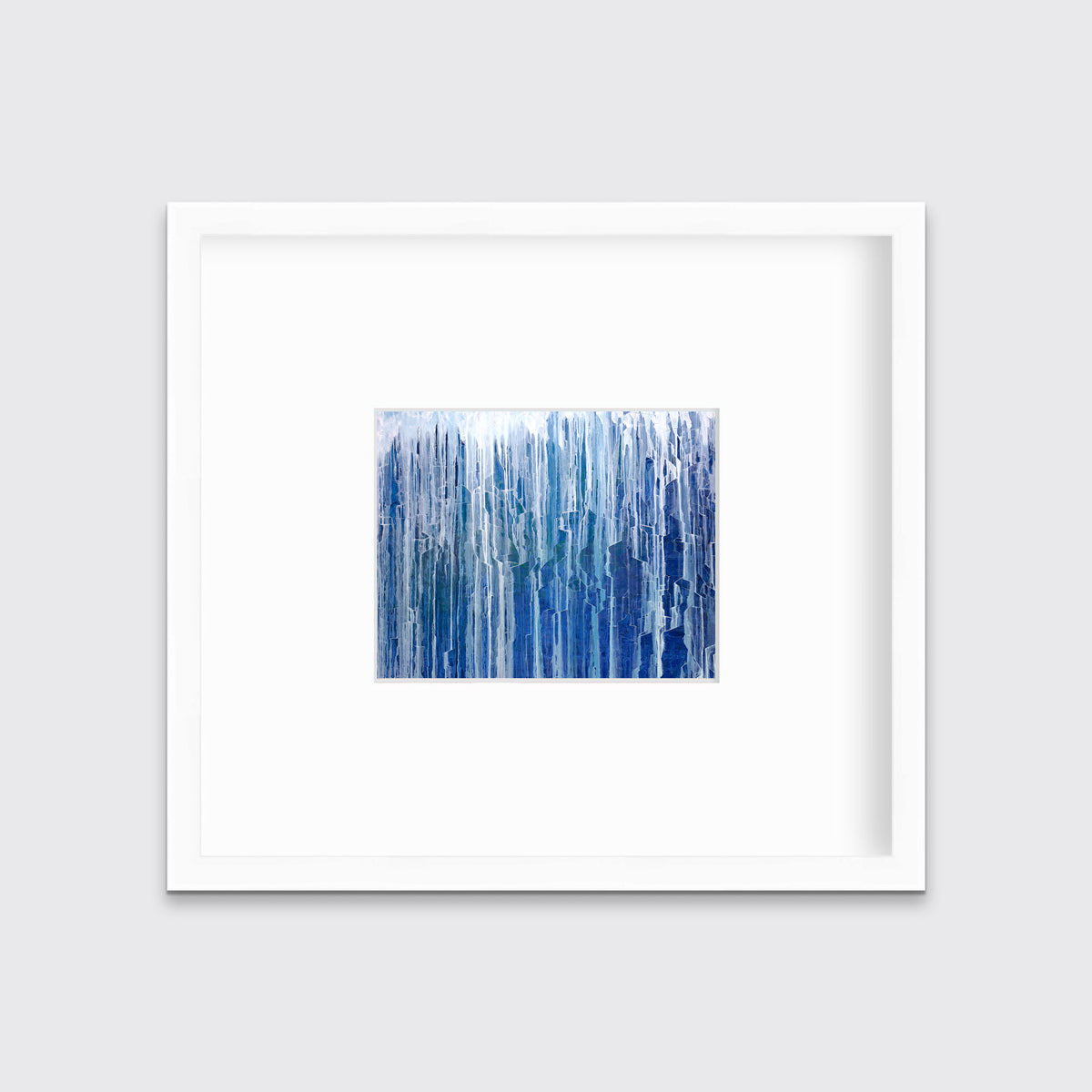 A blue and white abstract print in a white frame with a mat hangs on a white wall.