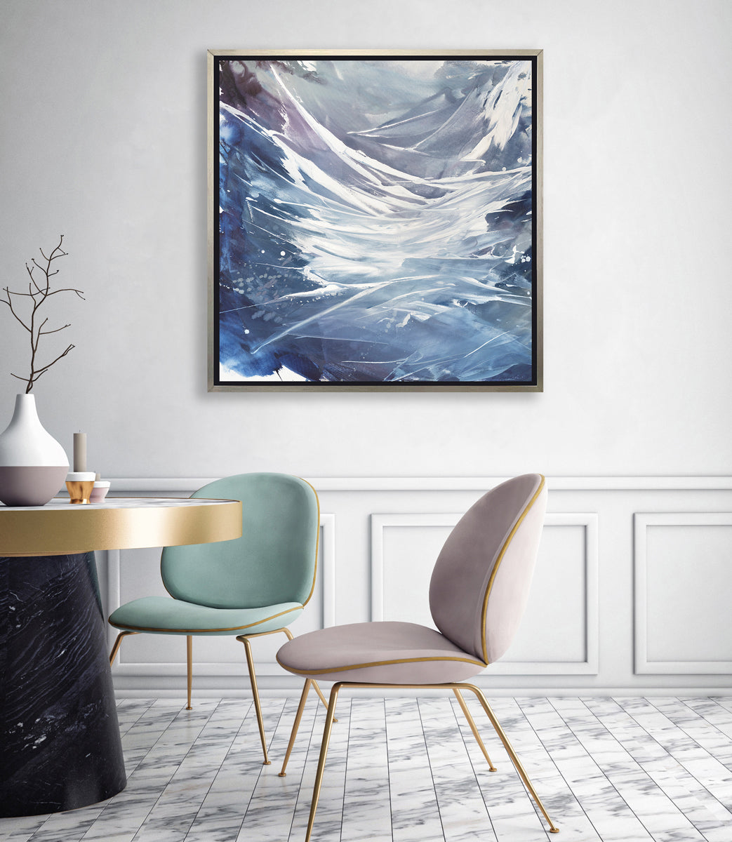 A light purple, grey, white and blue abstract print in a silver floater frame hangs on a white wall above a black and white marble pedestal table with a vase, a seafoam green chair and a light lavender chair.
