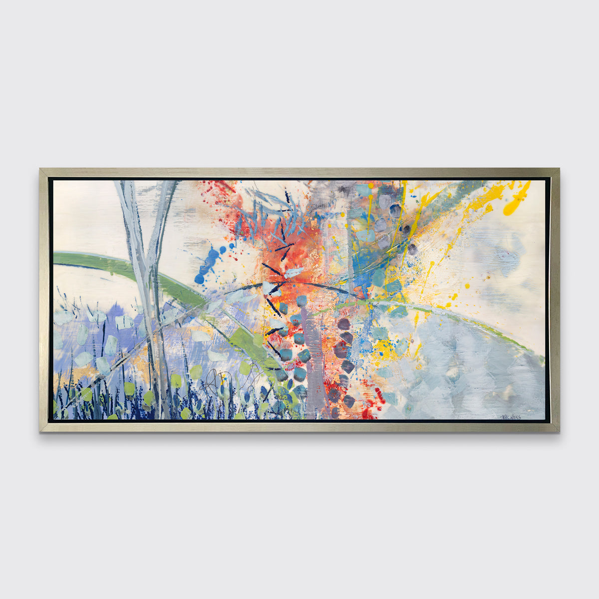 A multicolored abstract print in a silver floater frame hangs on a white wall.