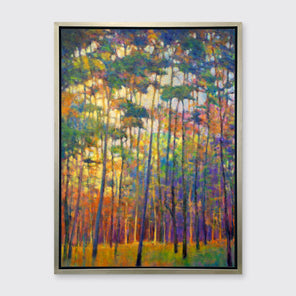 A multicolored abstract tree landscape print in a silver floater frame hangs on a white wall.