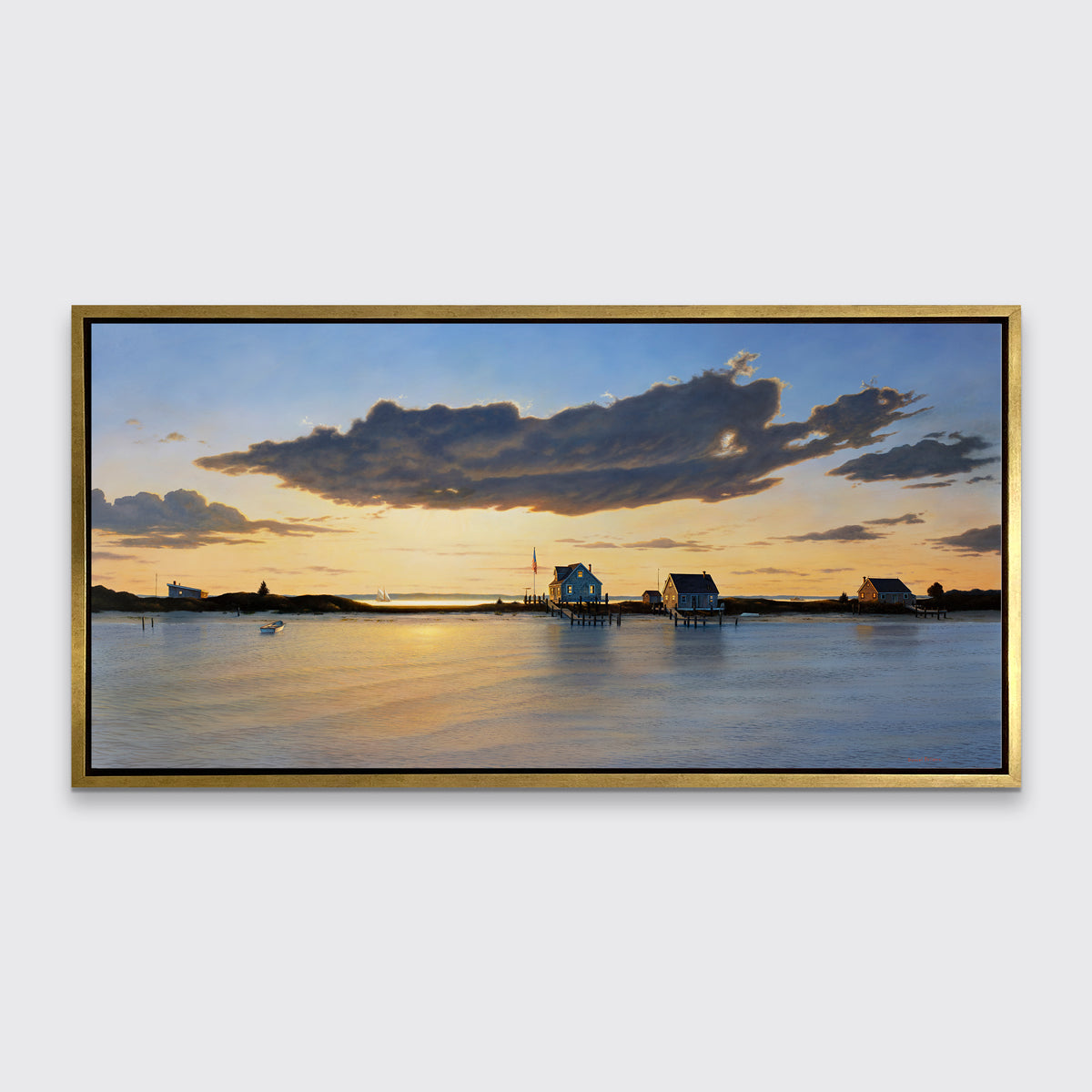 A print of three bay houses on a strip of land at sunset in a gold floater frame hangs on a white wall.
