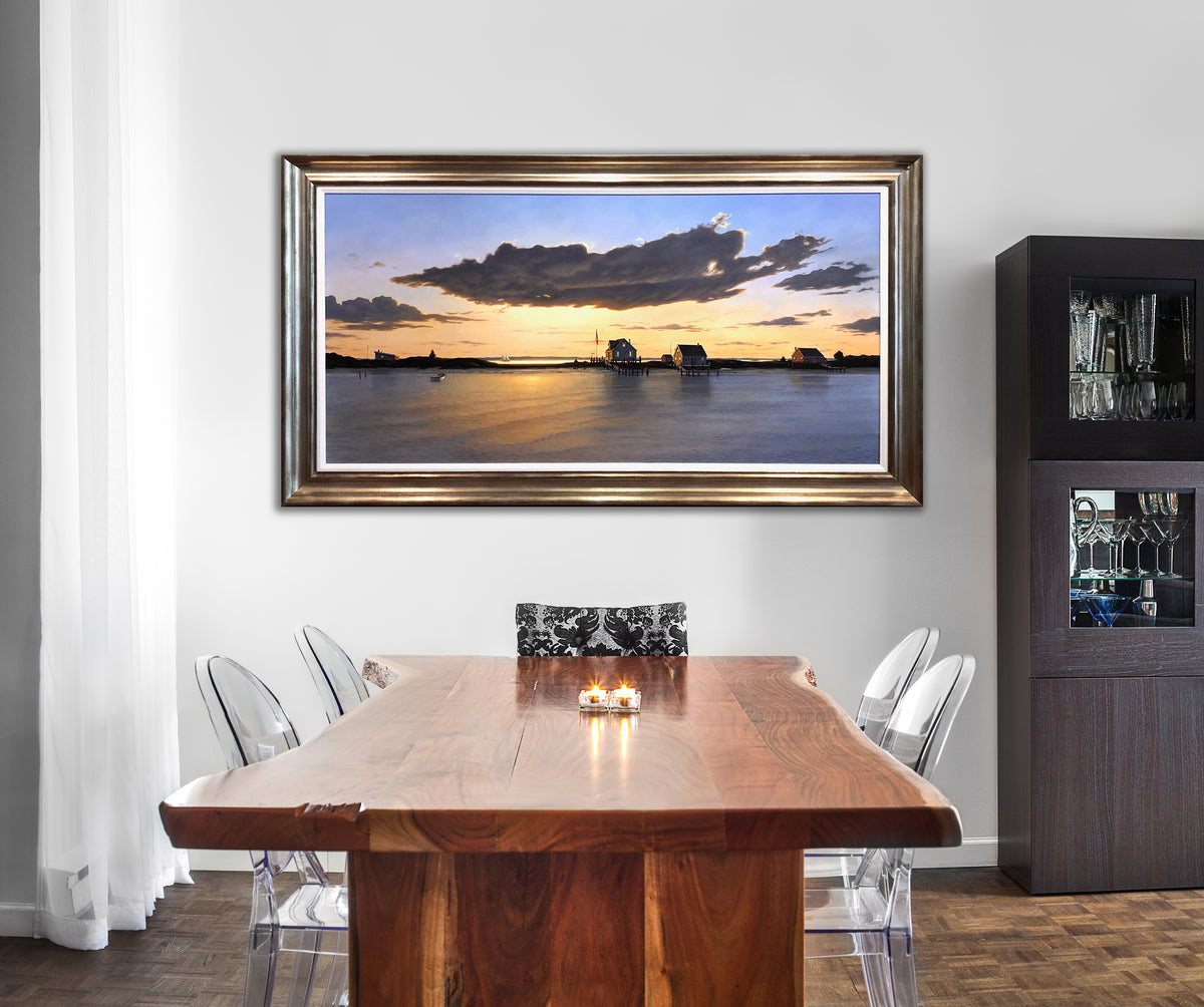 "Golden Meadows" framed and staged in a dining room on a white wall. The dinning room table is a natural cut piece of wood accompanied by clear plastic chairs.    
