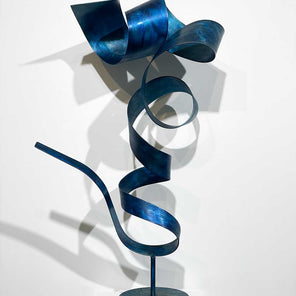 Abstract, steel sculpture with blue dye and wax sitting on a pedestal in front of a white wall.