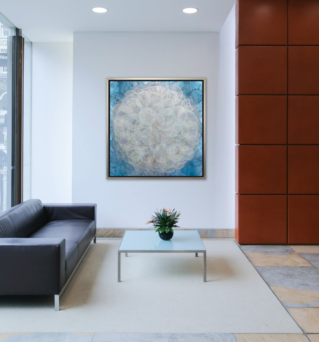 A blue, white, orange and yellow abstract geometric print in a silver floater frame hangs on a white wall above a black leather sofa and a square frosted glass coffee table with a potted floral arrangement.