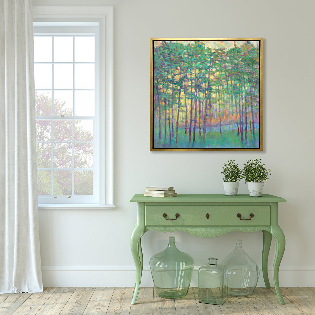 A green, yellow, orange and blue abstract tree landscape print in a gold floater frame hangs on a white wall above a green console table with a stack of books, two potted plants and three green glass bottles on the floor.