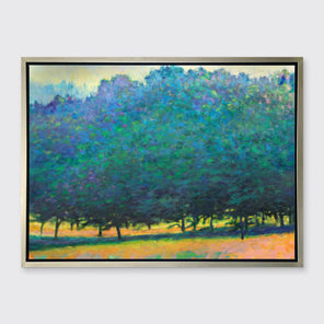 A green, orange and teal abstract tree landscape print in a silver floater frame hangs on a white wall.