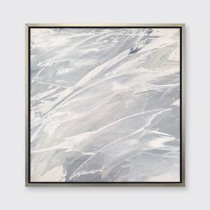 A grey, beige and white abstract print in a silver floater frame hangs on a white wall.