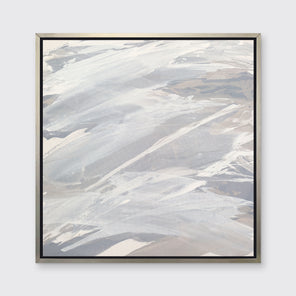 A grey, beige and white abstract print in a silver floater frame hangs on a white wall.