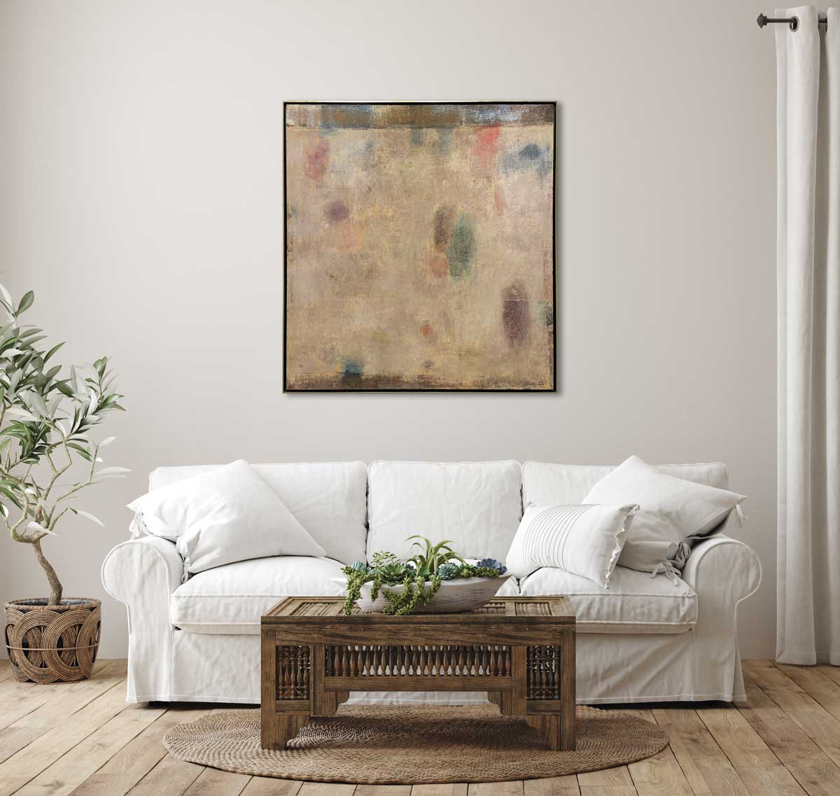 A beige painting with multicolored accents in a warm gold floater frame hangs on a white wall above a white sofa with pillows and an ornate wood coffee table with a succulent arrangement.