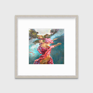 A teal, beige and red abstract distorted figurative print of a woman's body underwater with free flowing fabric in a silver frame with a mat hangs on a white wall.