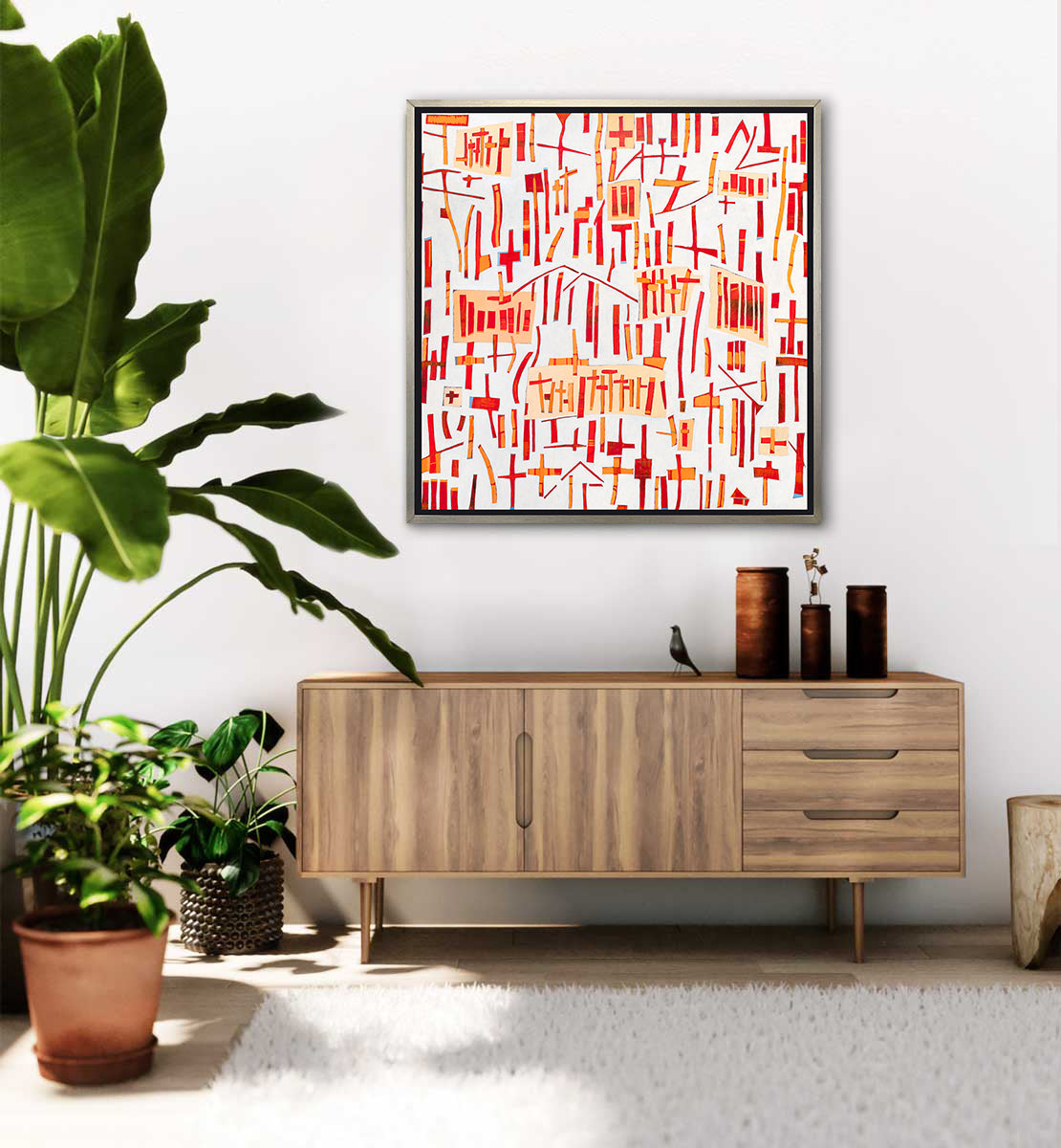A red, orange and white abstract print in a silver floater frame hangs on a white wall above a wooden cabinet with brown vases and several potted floor plants.