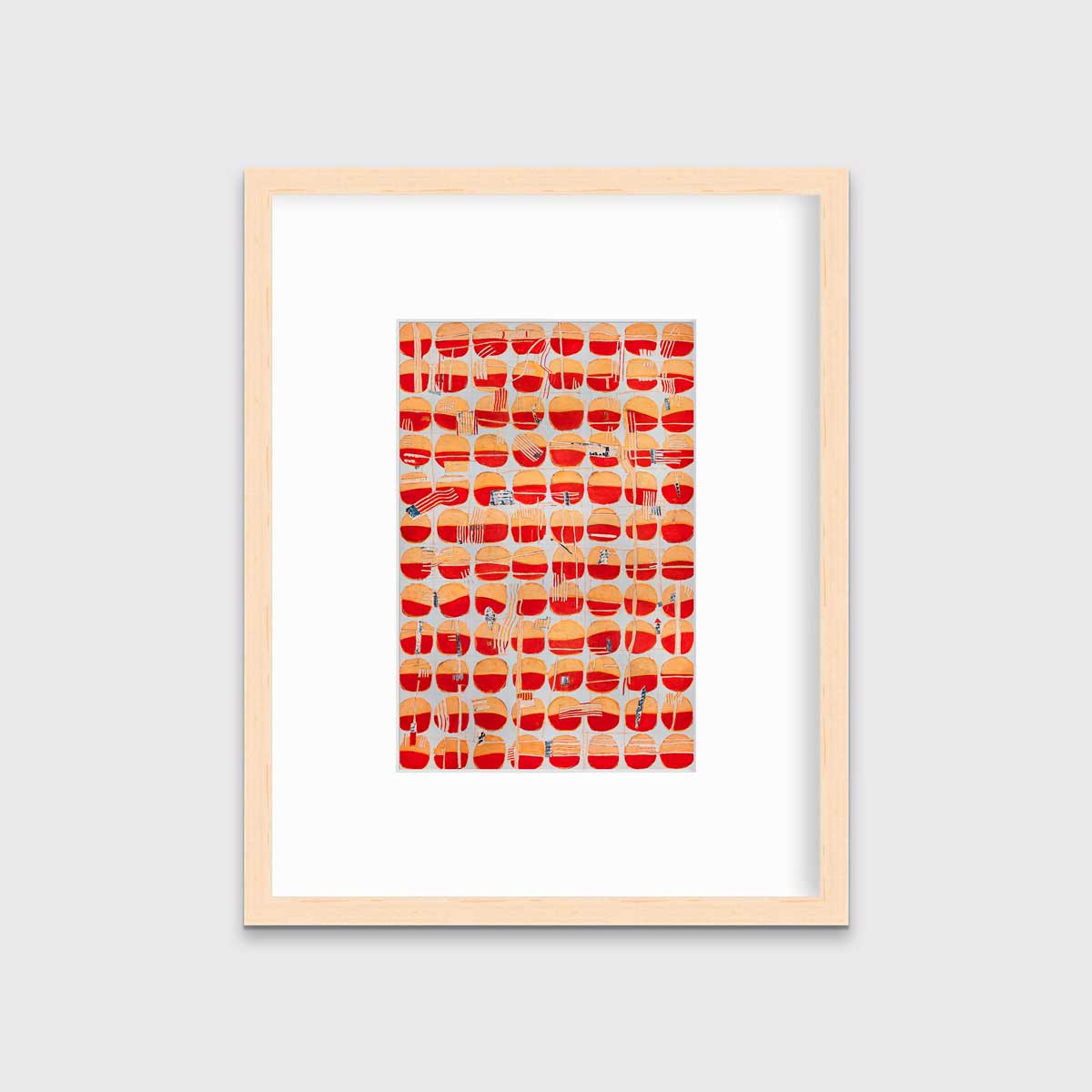 A red, orange and light blue abstract print in a natural wood frame with a mat hangs on a white wall.