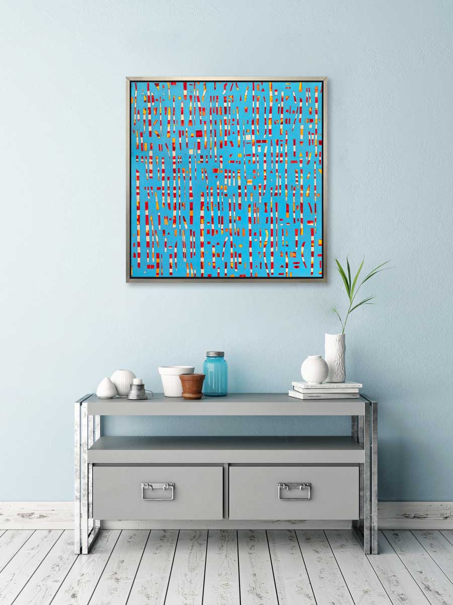 A blue, red, yellow and white abstract print in a silver floater frame hangs on a light blue wall above a grey console cabinet with white vases, a stack of books and small planters.
