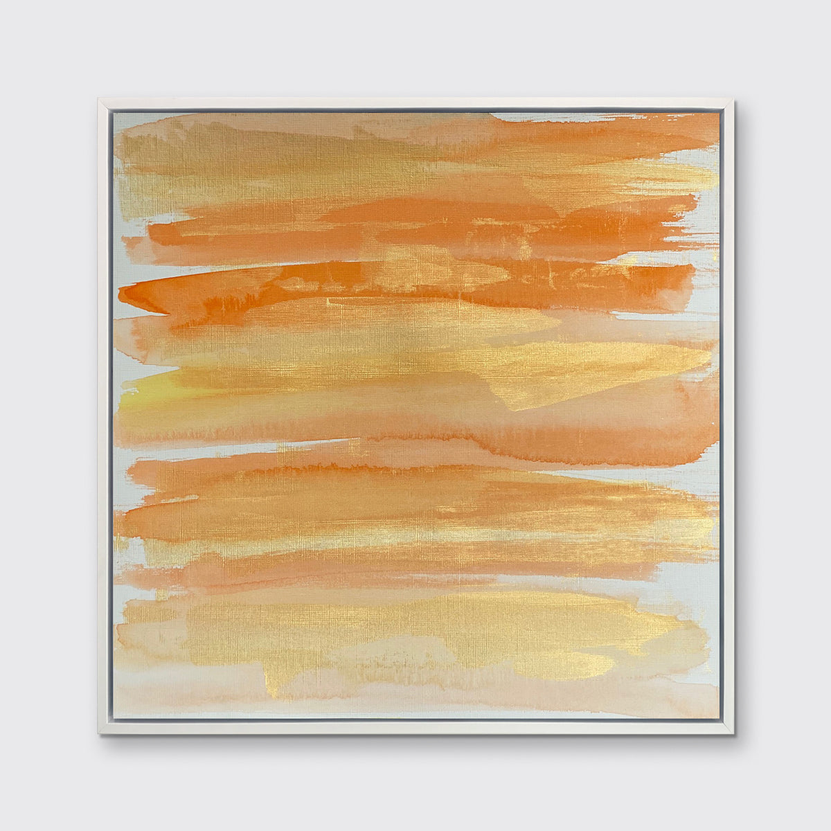 A orange, gold and white abstract print in a white floater frame hangs on a white wall.
