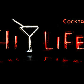 A photograph of a red and white neon sign that reads "Hi Life" and "cocktails" above it at night. 