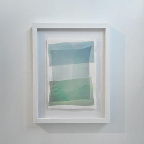 Tonal blues and green shapes overlap in this painting by Nealy Hauschildt in a white frame floating above a white matte hangs on a white wall.