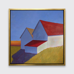 A white barn with a red roof print in a gold floater frame hangs on a white wall.