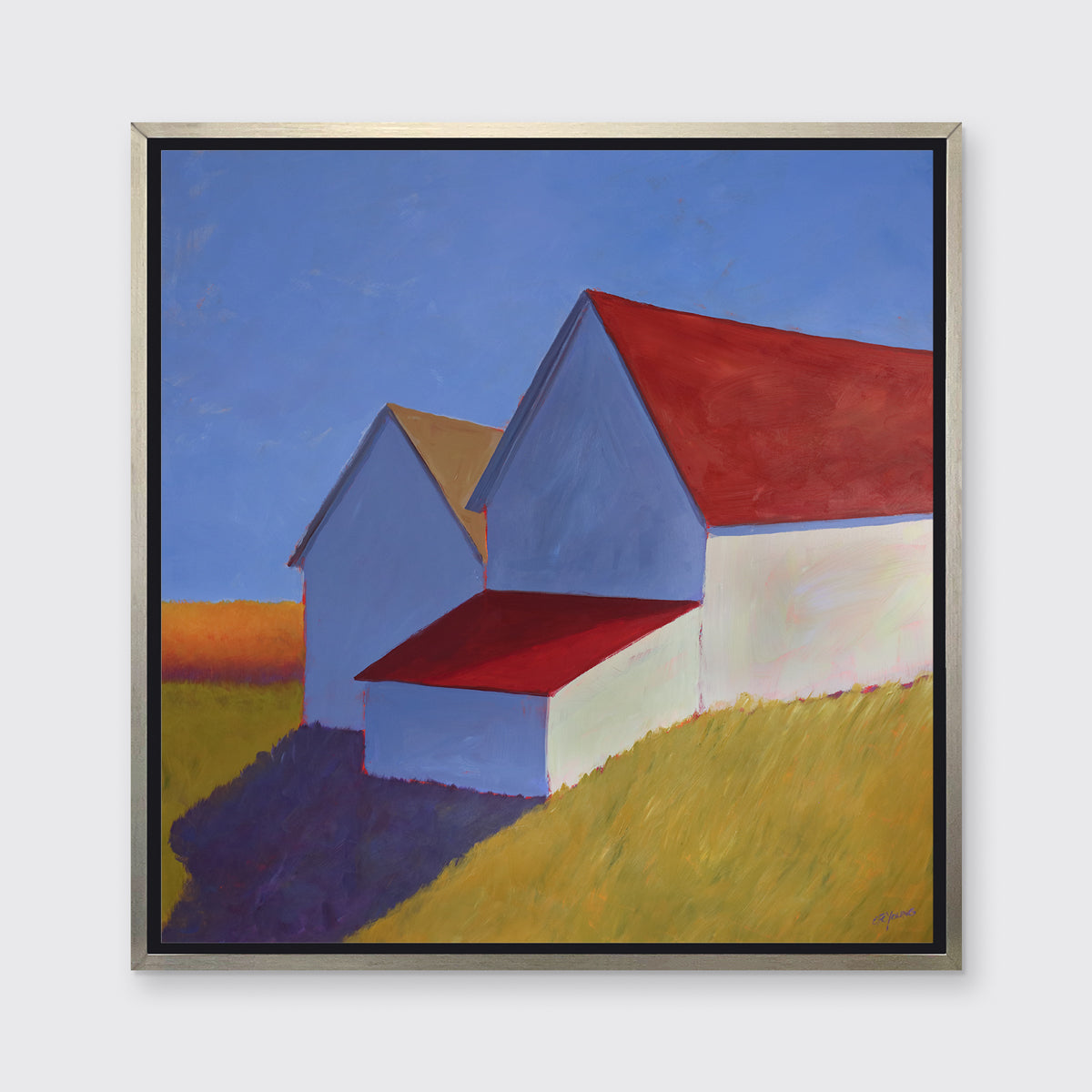A white barn with a red roof print in a silver floater frame hangs on a white wall.