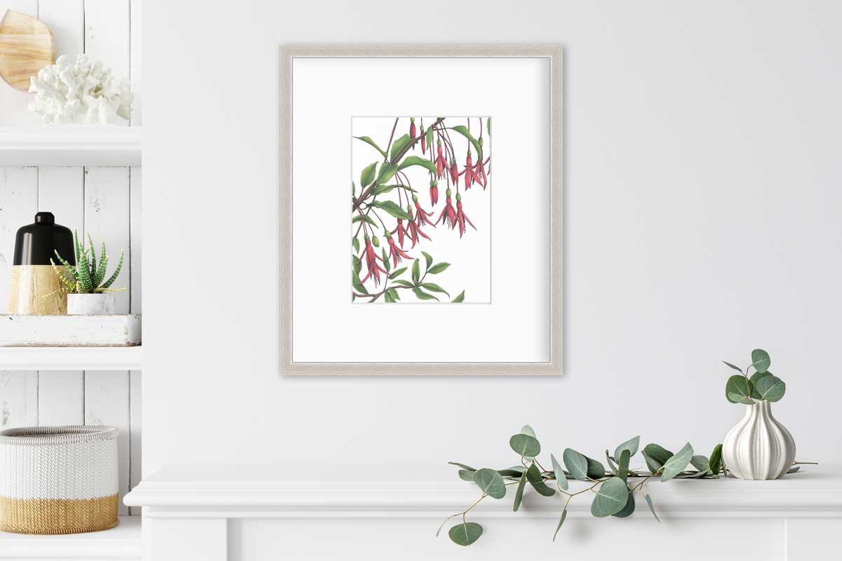 Red flowers with a brown stem and leaves print in a silver frame with a mat hangs on a white wall above a small plant in a vase and to the right of white floating shelves holding a variety of decor.