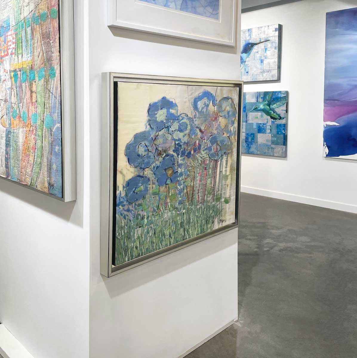 An abstract, encaustic floral painting of blue hydrangeas by Linda Bigness hangs on a white wall with a left side view. 