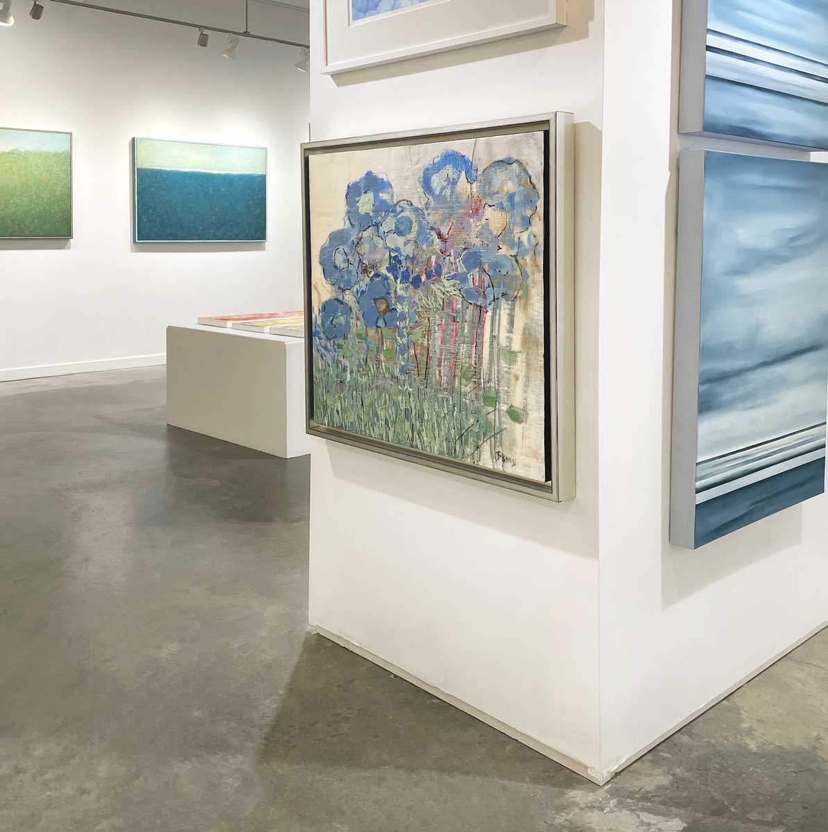 An abstract, encaustic floral painting of blue hydrangeas by Linda Bigness hangs on a white wall with a right side view. 