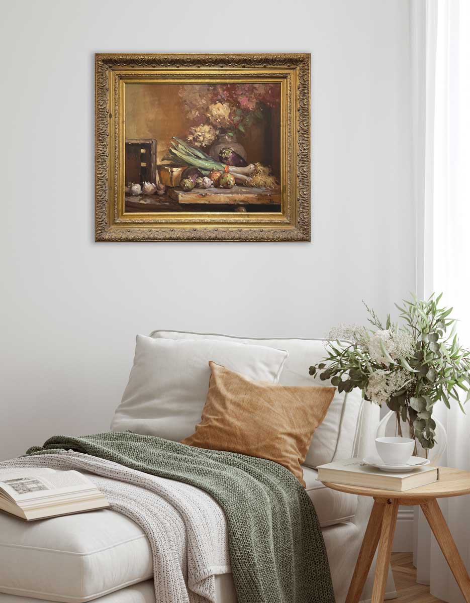 Hyperrealist painting of hydrangeas and vegetables on the table in a gold ornate frame hangs on a white wall above a light beige modern armless sofa with a green knit blanket and an orange pillow.