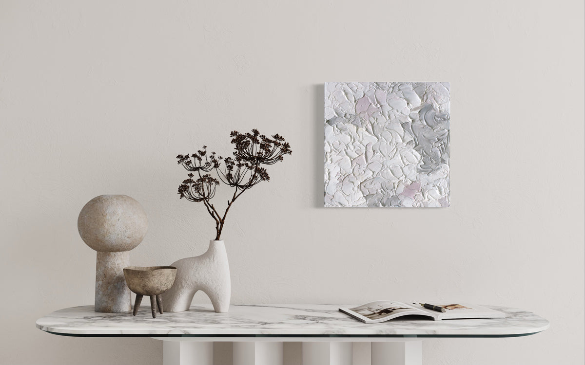 A small abstract painting hangs over a marble table.. 