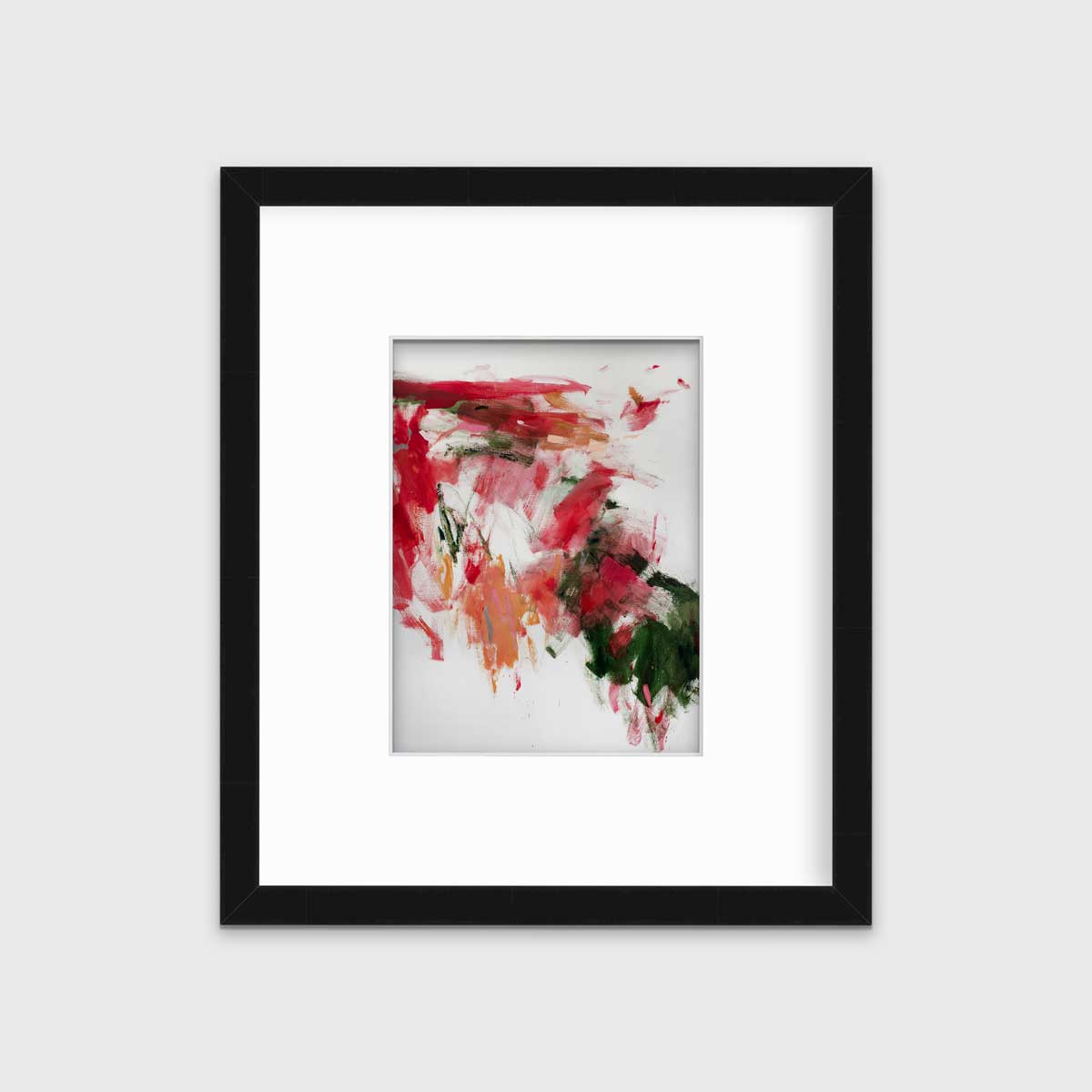 A red, green and white abstract print in a black frame with a mat hangs on a white wall.