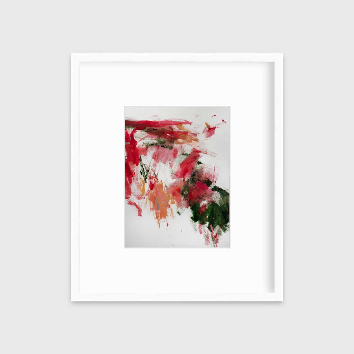 A red, green and white abstract print in a white frame with a mat hangs on a white wall.