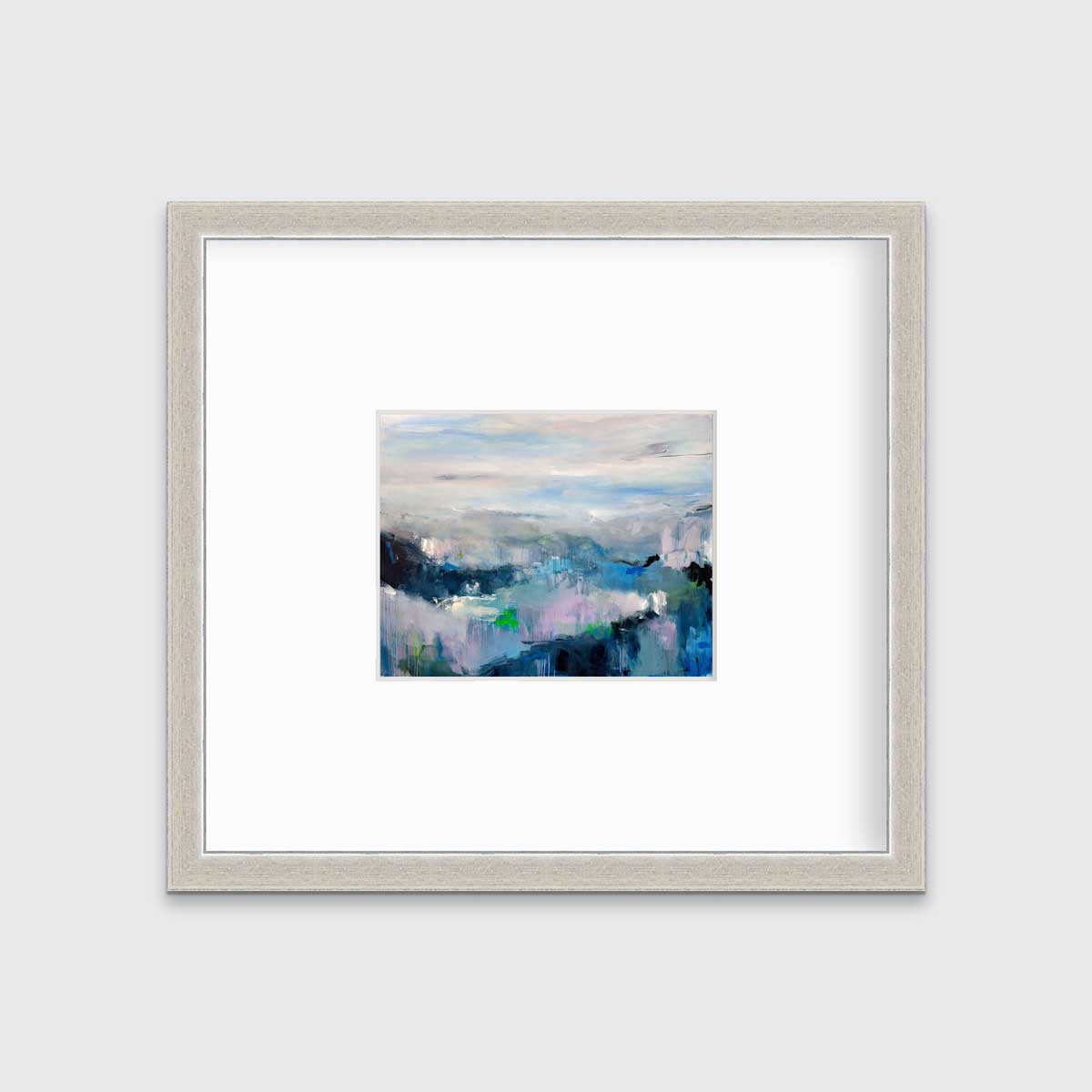 A blue abstract landscape by Kelly Rossetti in a silver frame with a mat hangs on a white wall.