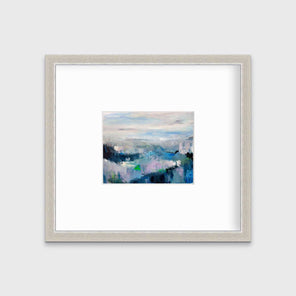 A blue abstract landscape by Kelly Rossetti in a silver frame with a mat hangs on a white wall.