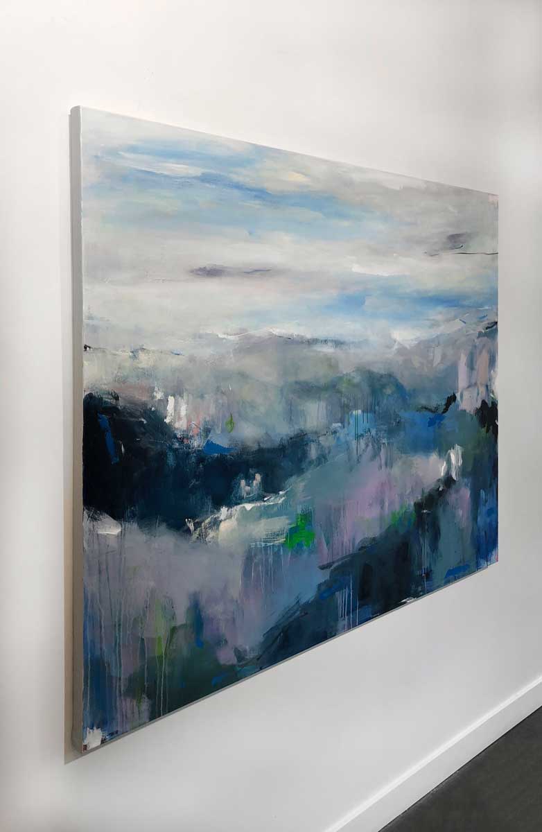 A left side-angle view of a blue and white abstract landscape painting hangs on a white wall.