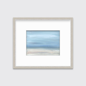 A white, blue and beige abstract seascape print in a silver frame with a mat hangs on a white wall.