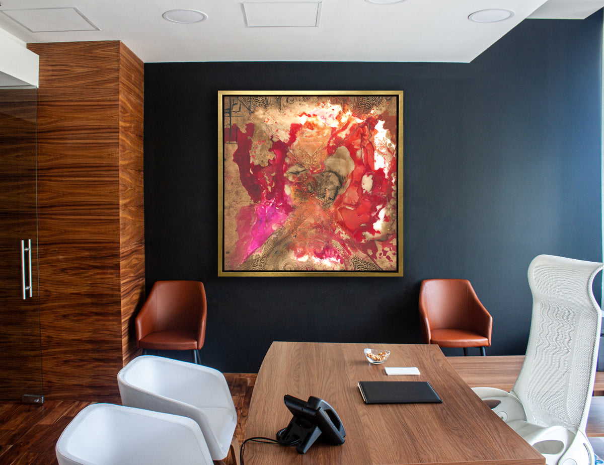 A gold, red and pink abstract print in a gold floater frame hangs on a navy blue wall above two brown leather chairs and across from a wood desk with two matching white chairs and a white high back desk chair.