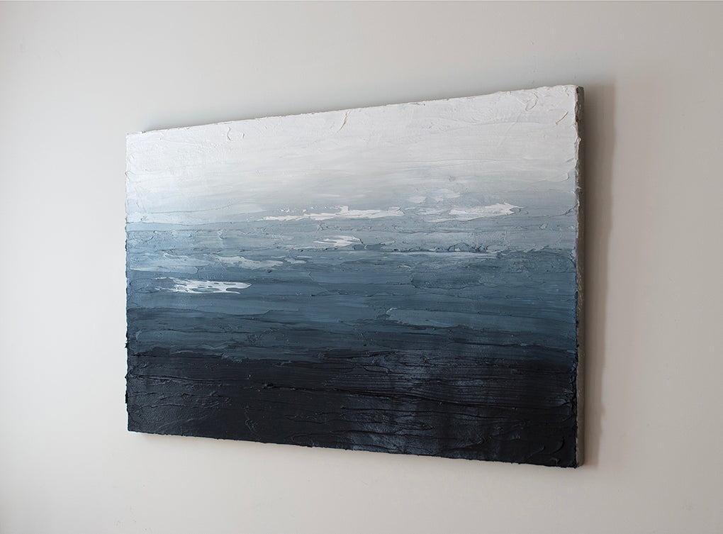 A side view blue, white and navy very textured abstract painting hangs on a white wall.