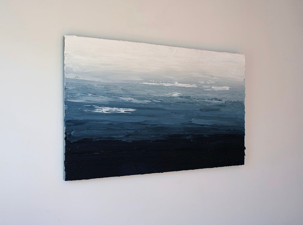 A side view blue, white and navy very textured abstract painting hangs on a white wall.