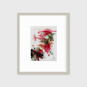 A red, green and white abstract print in a silver frame with a mat hangs on a white wall.