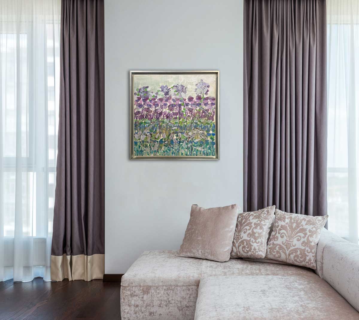 An abstract, encaustic floral painting of purple irises by Linda Bigness hangs on a white wall in between windows with muted purple curtains above a muted pink velvet sectional. 