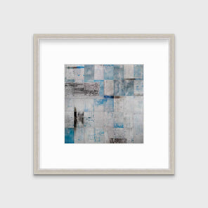 A blue, grey and black abstract print in a silver frame with a mat hangs on a white wall.
