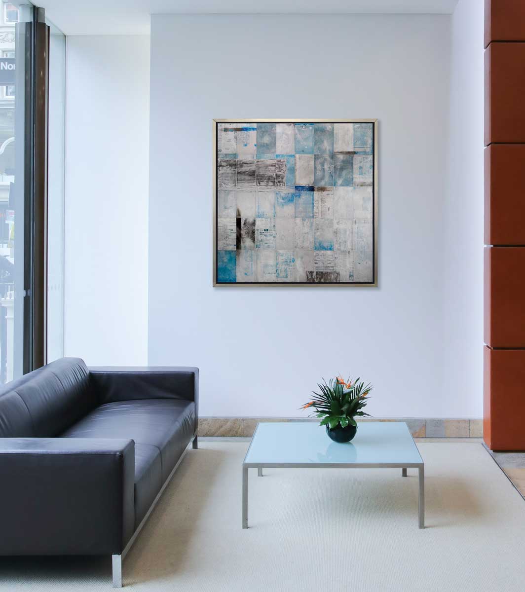 A blue, grey and black abstract print in a silver floater frame hangs on a white wall above a black sofa and a square coffee table with a floral arrangement.