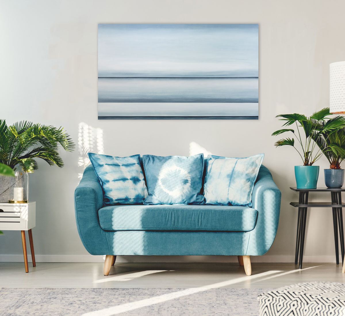 A blue oil painting with multiple navy lines dividing the canvas that suggest horizon lines is hung above a loveseat. Wired and ready to hang.