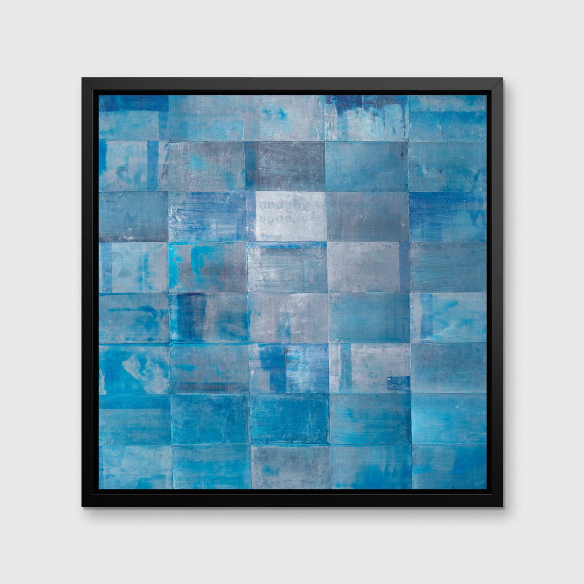 A blue geometric print in a black floater frame hangs on a white wall.