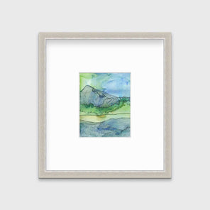 A blue and green landscape illustration print framed in a silver frame with a mat hangs on a light grey wall.