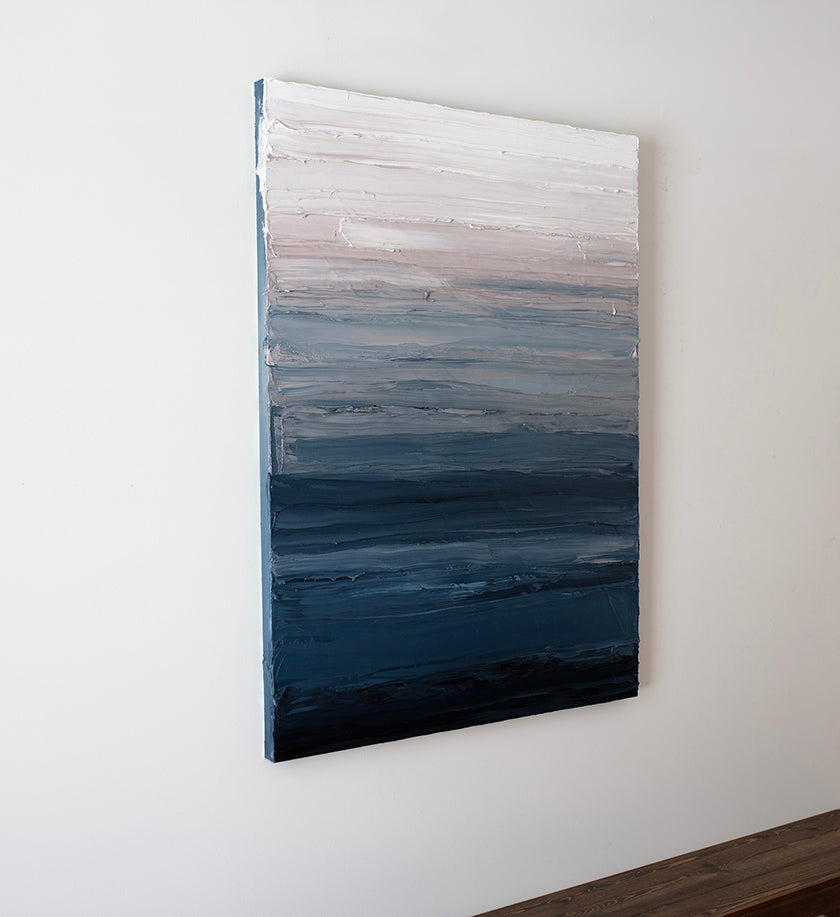 A left side-view of a tonal blue, light pink and white textured abstract painting hangs on a white wall.