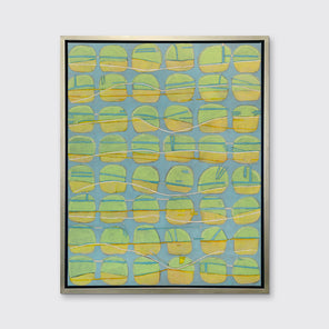 A yellow, green and light slate blue abstract circle print in a silver floater frame hangs on a white wall.