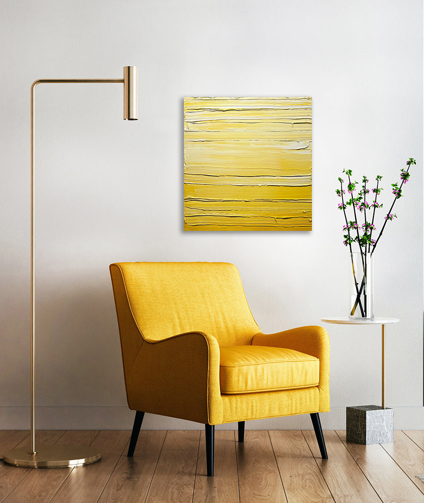 A textured yellow toned painting hangs on a white wall above a yellow chair and a round white table with a vase of flowers..