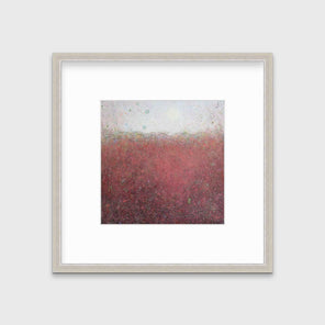 A red abstract landscape print in a silver frame with a mat hangs on a white wall.