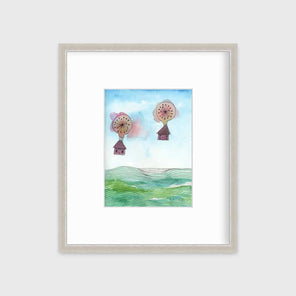 A hot air balloon and house illustration print in a silver frame with a mat hangs on a light grey wall.