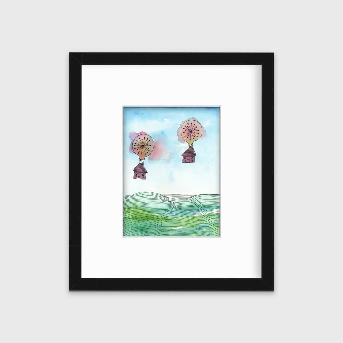 A hot air balloon and house illustration print in a black frame with a mat hangs on a white wall.
